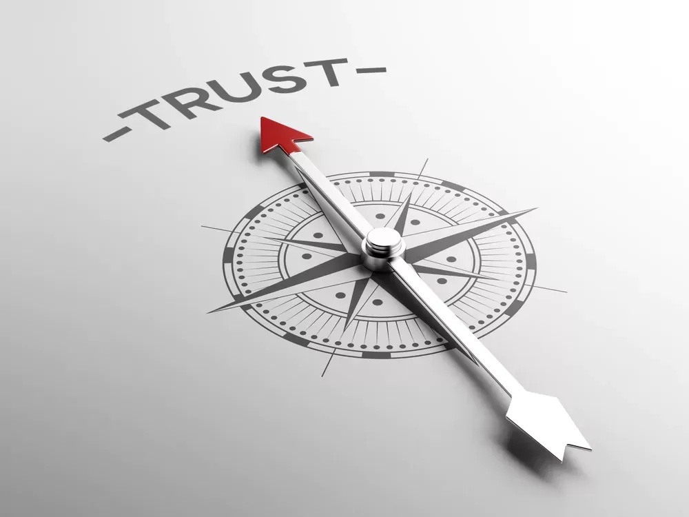 Een kompas op een lichte ondergrond, met de naald wijzend naar het woord "trust" erboven.
